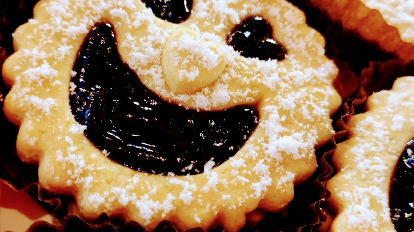 A round shortbread biscuit with a jam smiley face, dusted with icing sugar